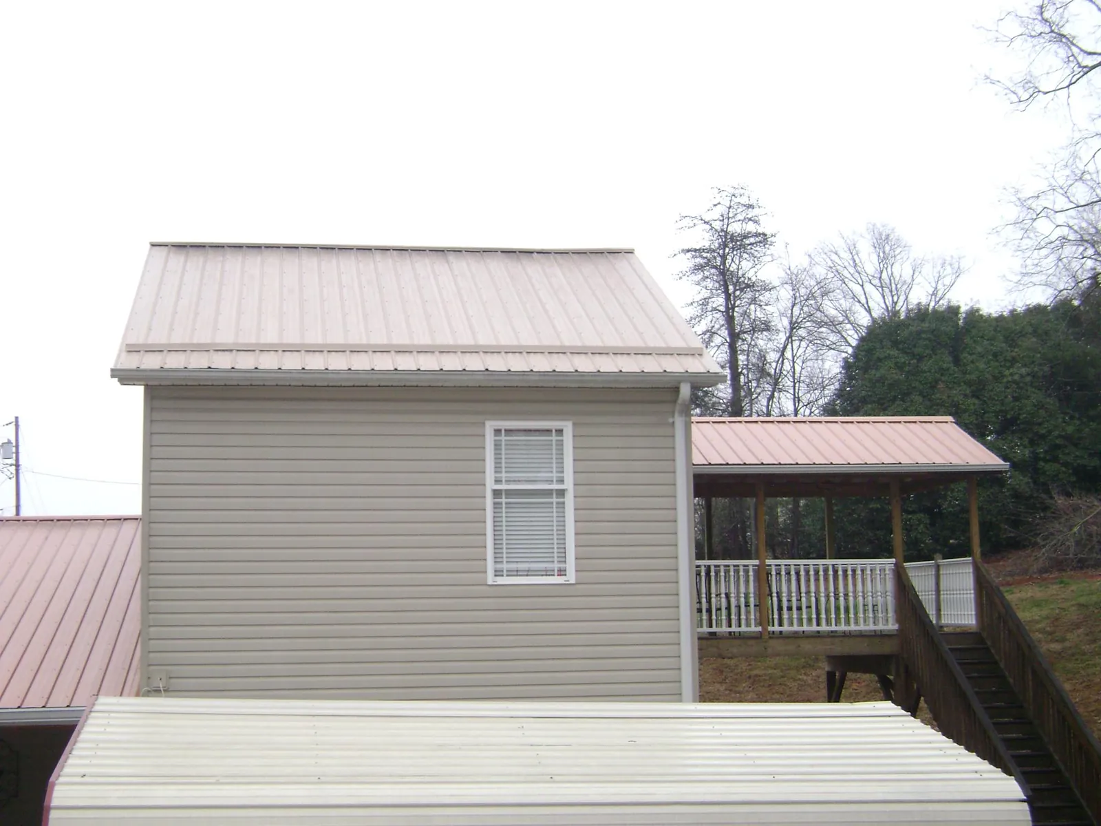 Tan metal roofs on a two story addition and attached porch, from a Roof Replacement job in Eufaula